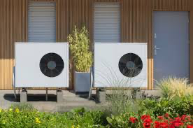 Dual air source heat pump units installed on the exterior of an eco-friendly modern UK home, surrounded by garden plants.